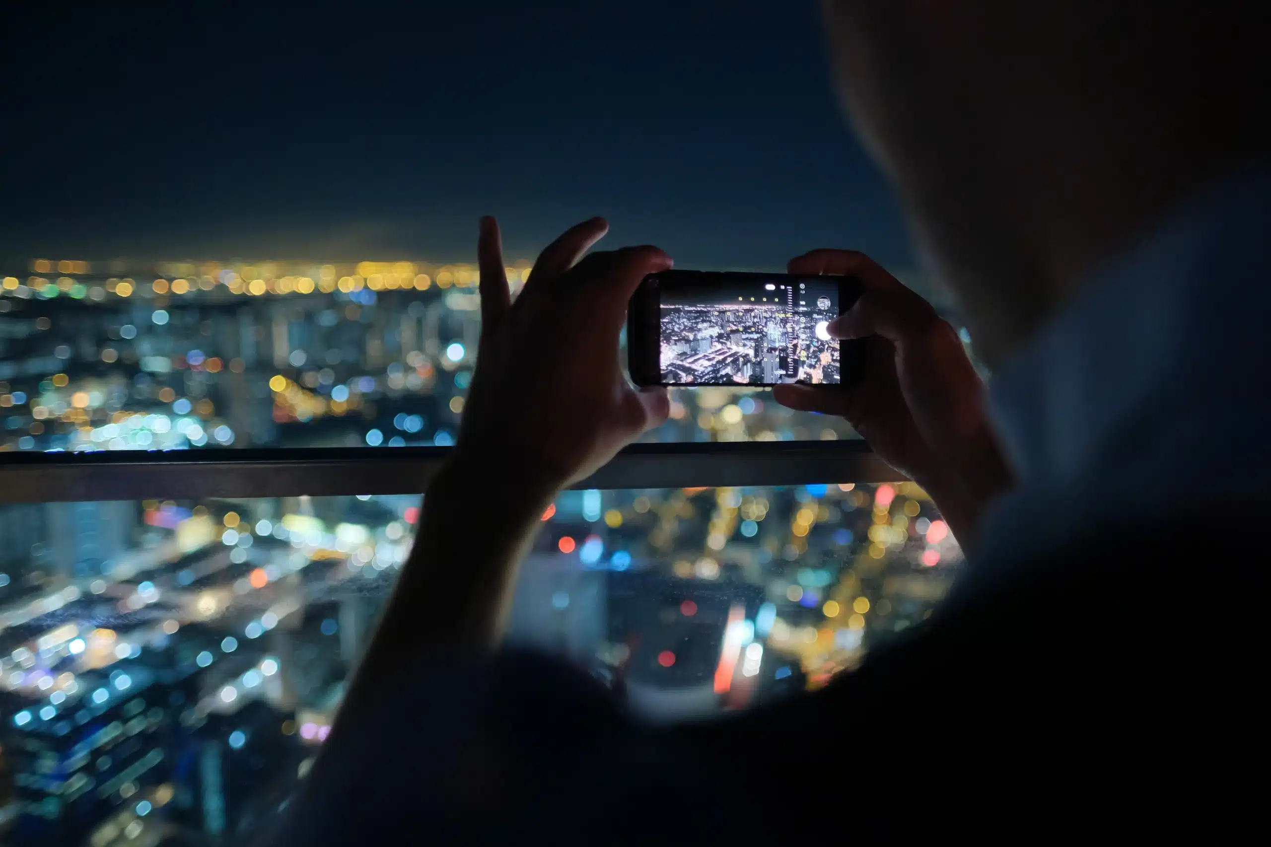 Person photographing night cityscape with smartphone.
