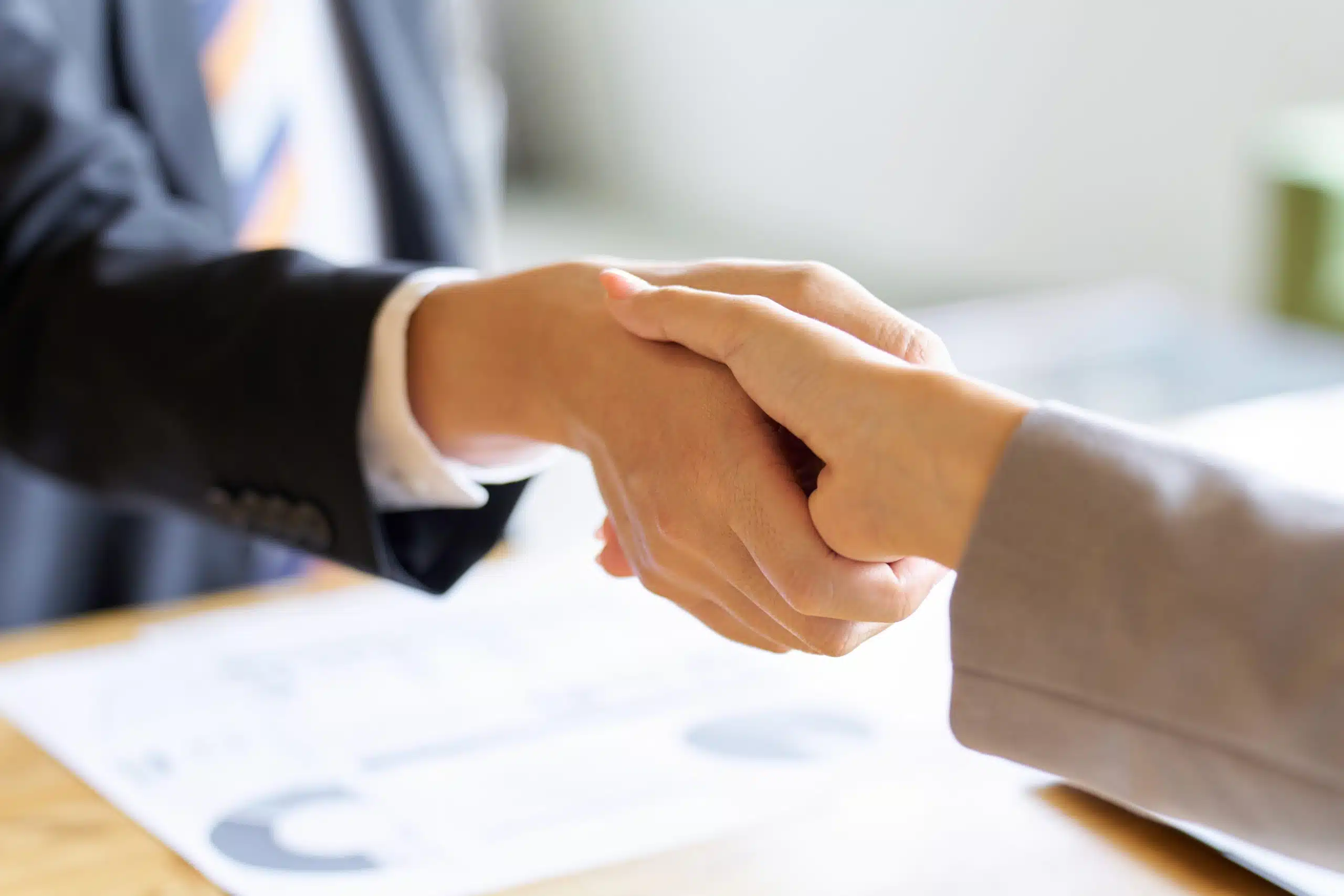 Business handshake over documents on desk.