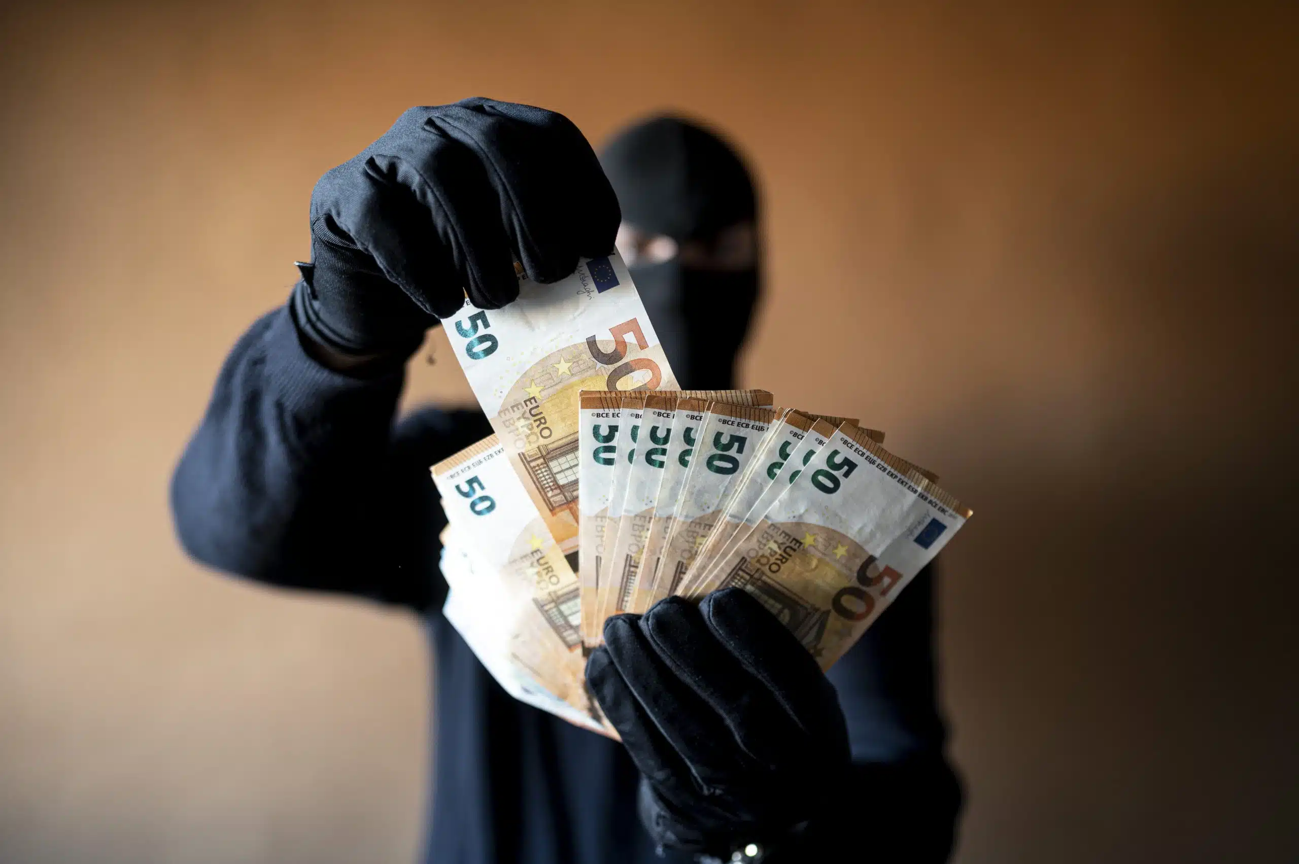 Person in gloves holding €50 notes, obscured face.