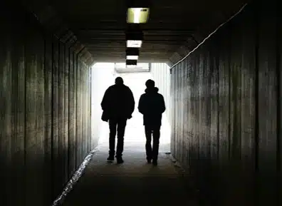 Two people walking through a dimly lit tunnel.