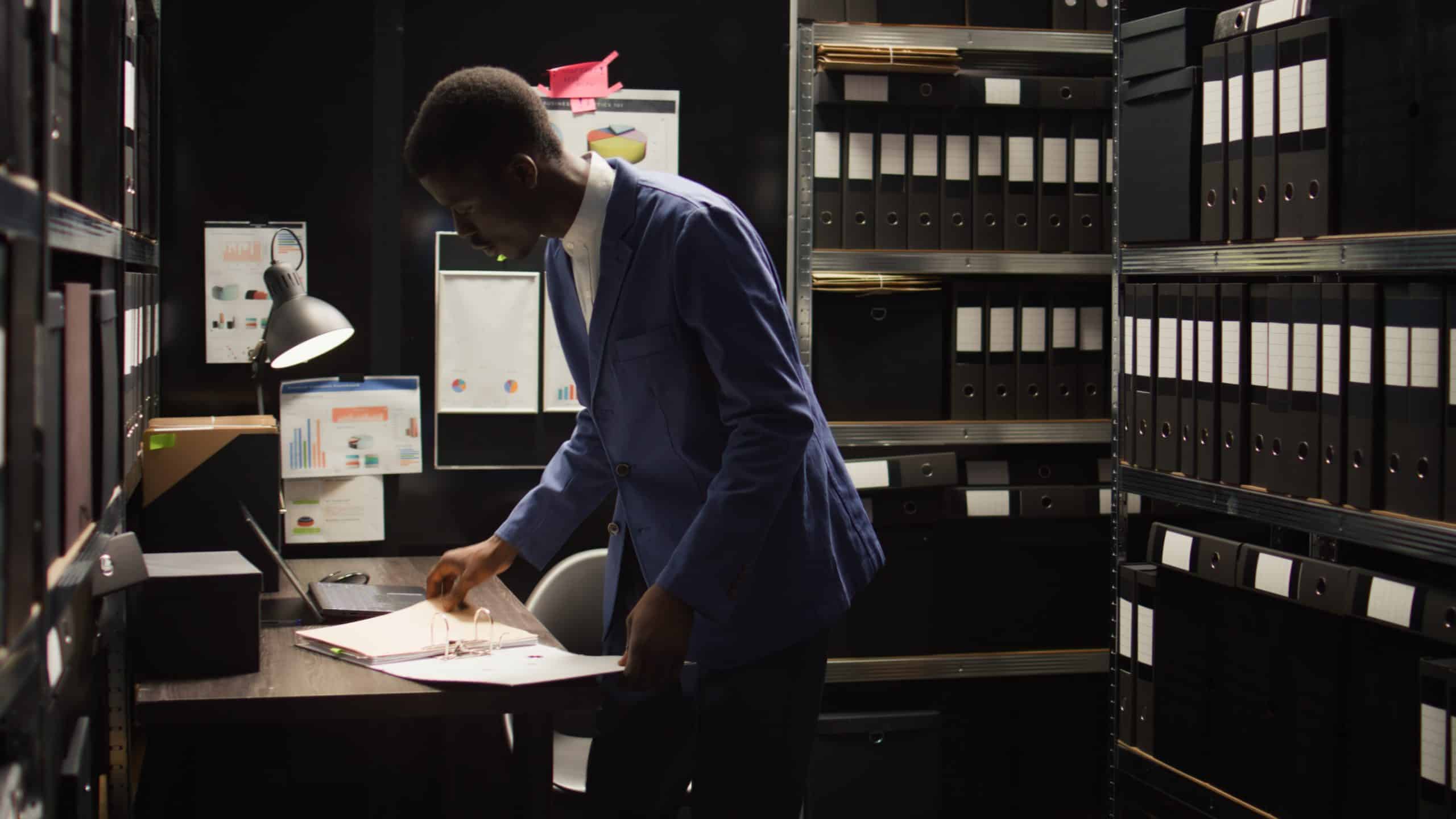 Man organizing paperwork in dimly lit office.