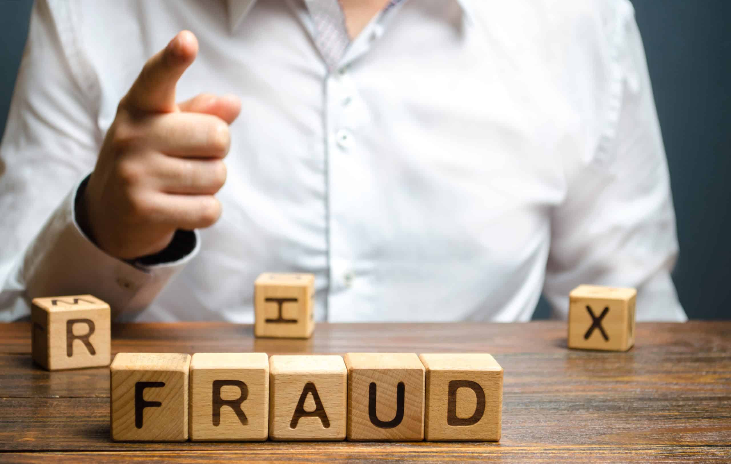 Person highlighting fraud with finger and blocks.