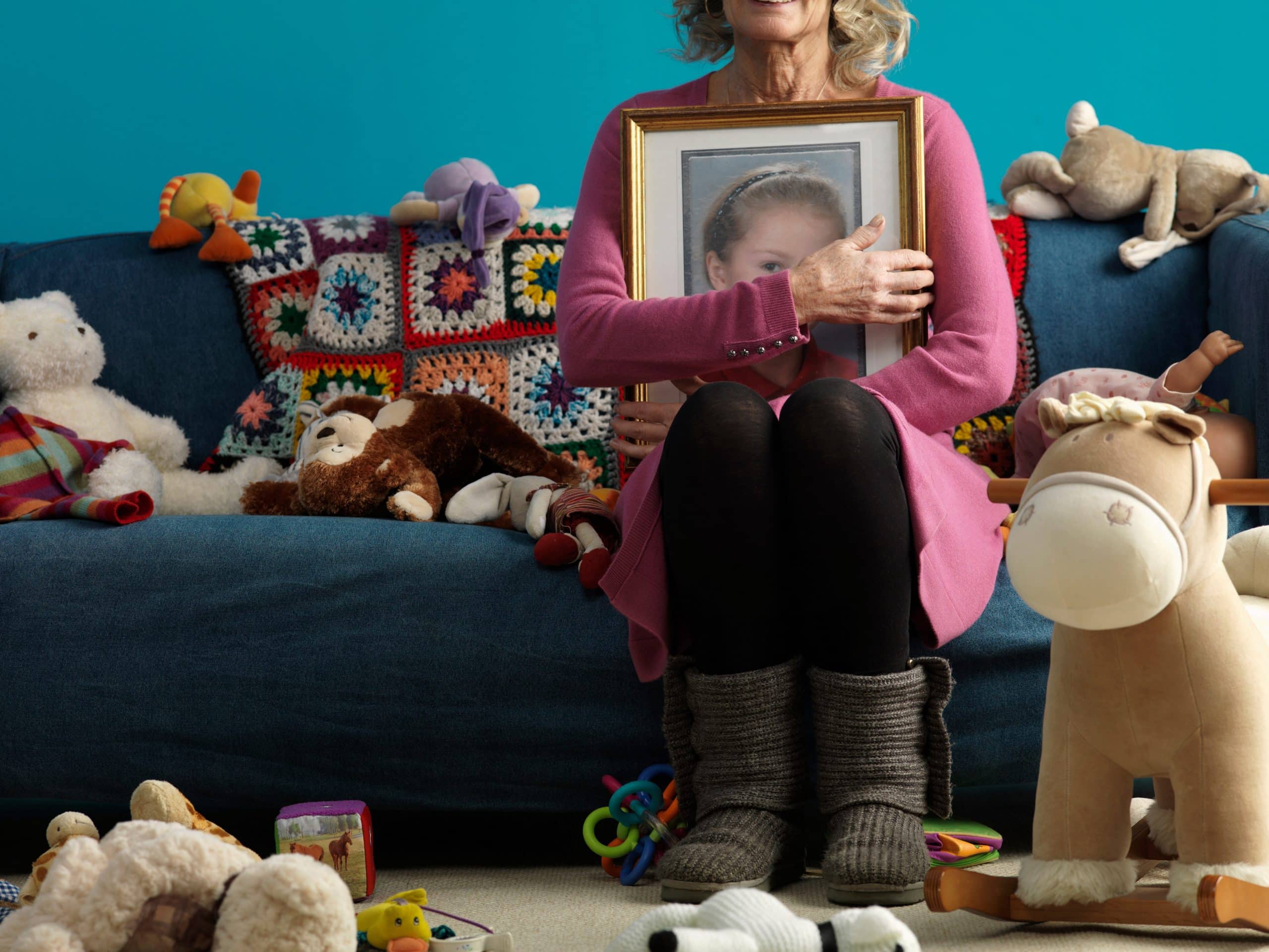 Woman holding portrait surrounded by toys on couch.
